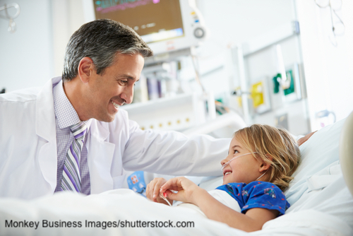 Arzt mit weißem Kittel lächelt ein im Krankenbett zurück lächelndes Kind an